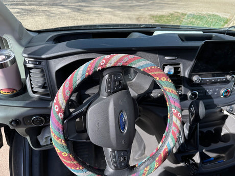 Dashboard of an RV rental, showing a Ford steering wheel with a colorful, patterned cover and a large touchscreen display.