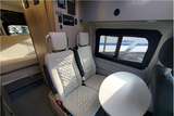 Experience an **RV rental**! Modern camper van interior features two quilted seats, a table, and a rear bed area.
