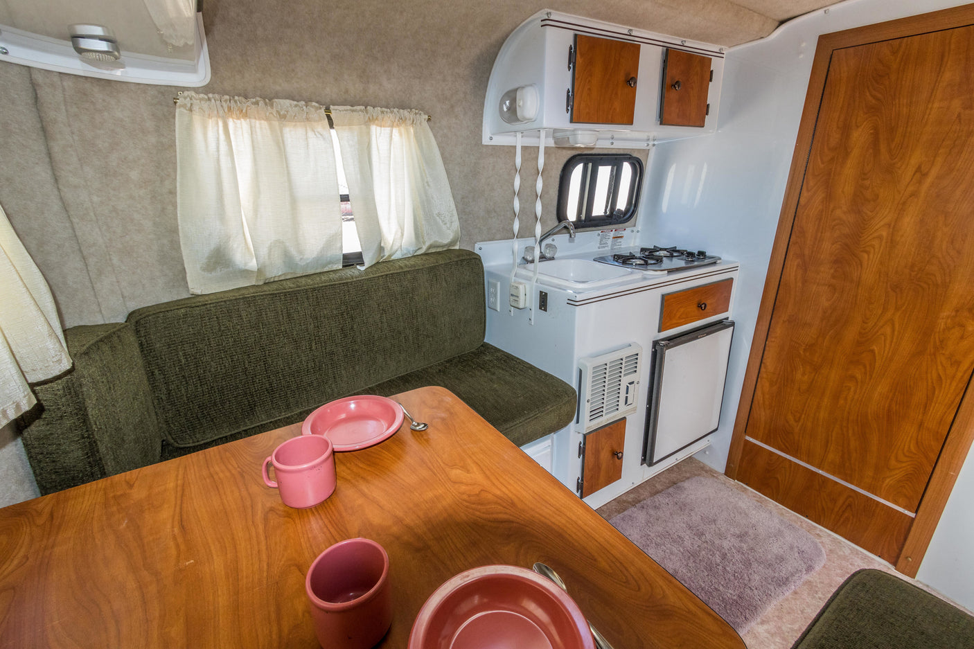 Cozy rv rental interior: kitchenette, dining area with pink dishes, and comfy green seating for your travels.