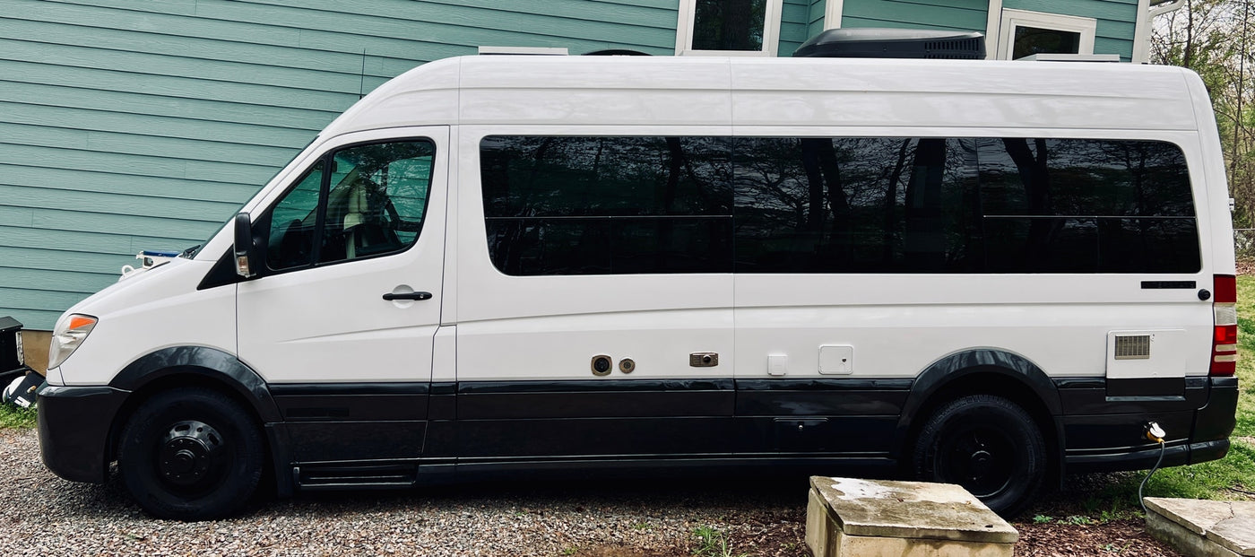 parked on gravel next to a light blue house.|Front view of a white Mercedes Sprinter van with a custom "VANDALF" plate. Ideal for an RV rental