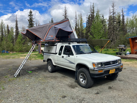 White pickup truck with a deployed rooftop tent, offering an RV rental alternative for camping and overlanding in Alaska.