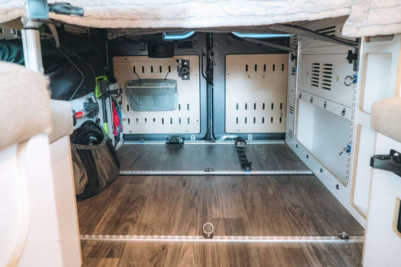 Organized under-bed storage in an RV rental camper van, featuring modular panels, LED lighting, and tie-downs for travel gear.