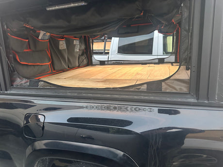 Inside an RV rental truck bed camper: organized storage pockets line the side, above a wooden sleeping platform.