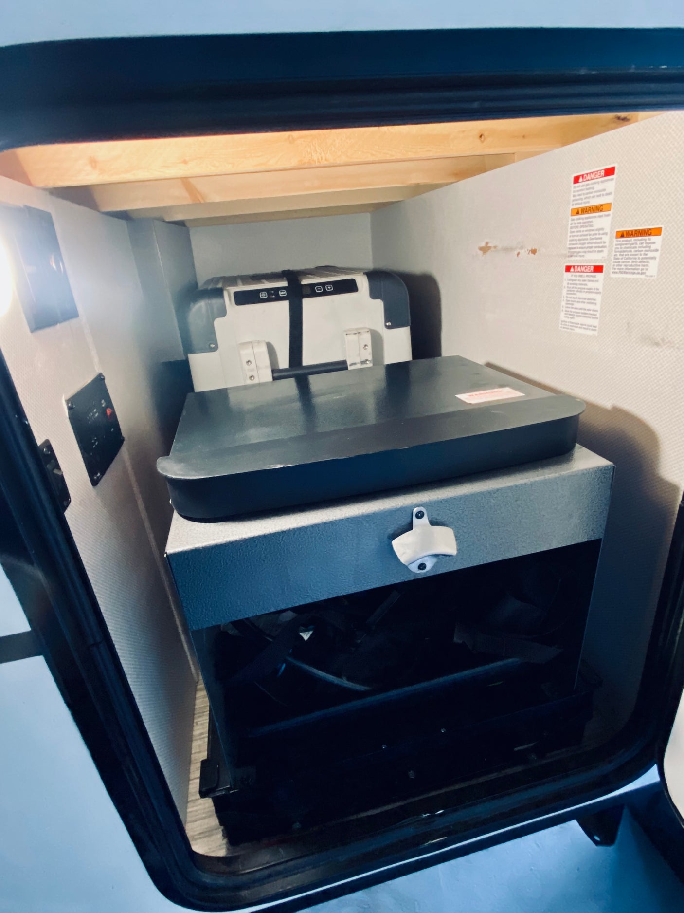 RV rental: Interior storage bay with a portable cooler/fridge, organized gear, and a mounted bottle opener.