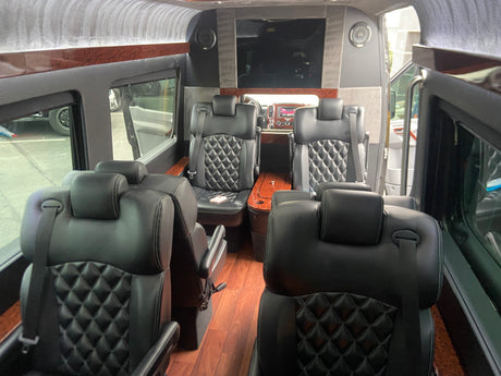 Luxurious RV rental interior: black leather diamond-stitched seats, wood trim, and a large entertainment screen.