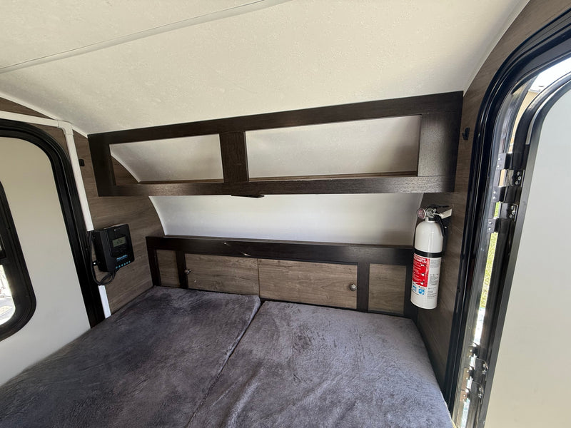 This RV rental interior offers a cozy bed, overhead cabinets, a solar charge controller, and a fire extinguisher for safety. — photo 3