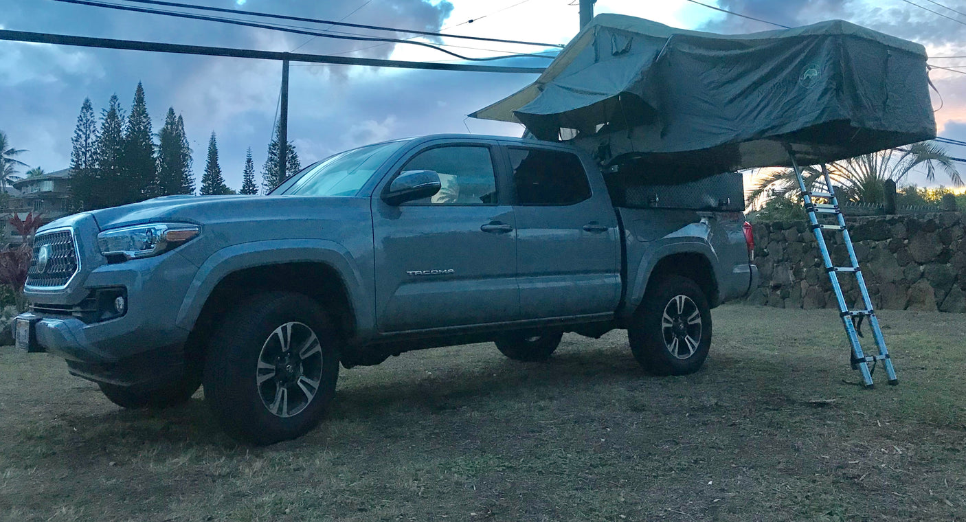 Grey pickup truck with a deployed rooftop tent and ladder, perfect for an **RV rental** adventure.