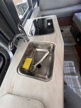 Inside an RV rental: Compact kitchenette with stainless steel sink, faucet, and cooktop. Featuring cozy sofa seating.