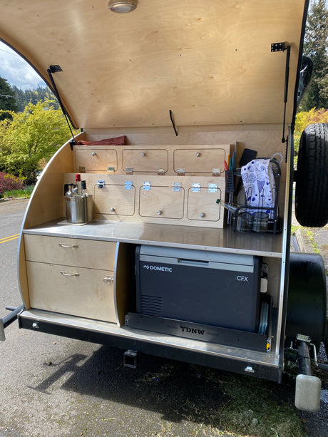 Explore this cozy teardrop camper's galley, perfect for an RV rental. It has a Dometic fridge, pull-out storage, and full kitchen setup.