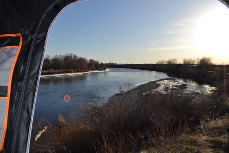 Cozy river view from an RV rental, with bare trees & snowy banks. Ideal for a winter escape.