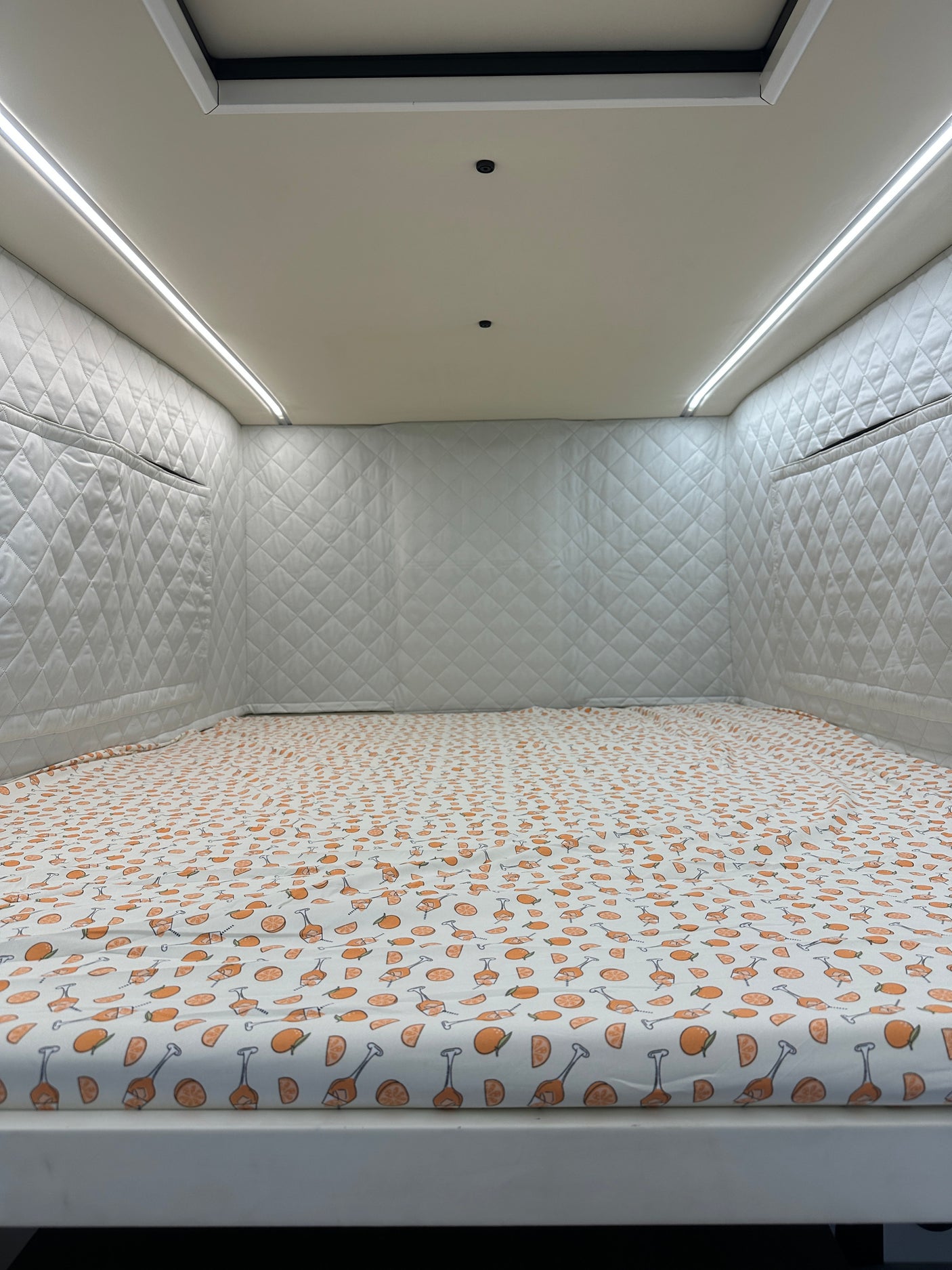 Cozy RV rental interior featuring a bed with vibrant citrus sheets, soft quilted walls, and bright ambient LED lighting.