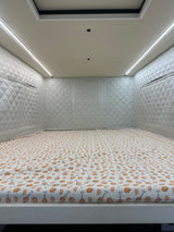 Cozy RV rental interior featuring a bed with vibrant citrus sheets, soft quilted walls, and bright ambient LED lighting.