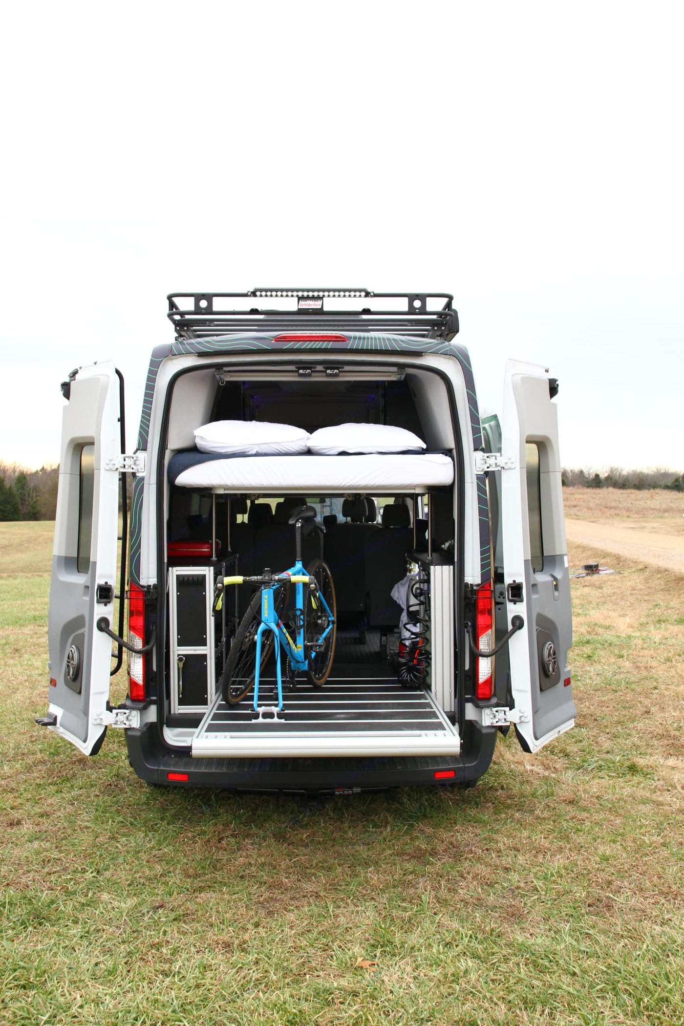  parked on dry grass before the Grand Teton mountains.|Overhead view: an RV rental van is parked on grassy hill beside a lake