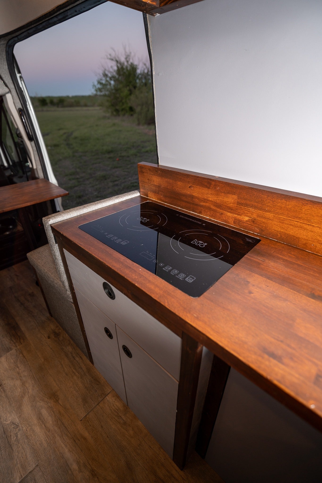 Compact RV rental kitchen with an induction cooktop and warm wood counters, perfect for mobile living.