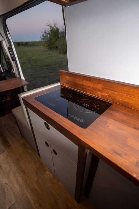 Compact RV rental kitchen with an induction cooktop and warm wood counters, perfect for mobile living.