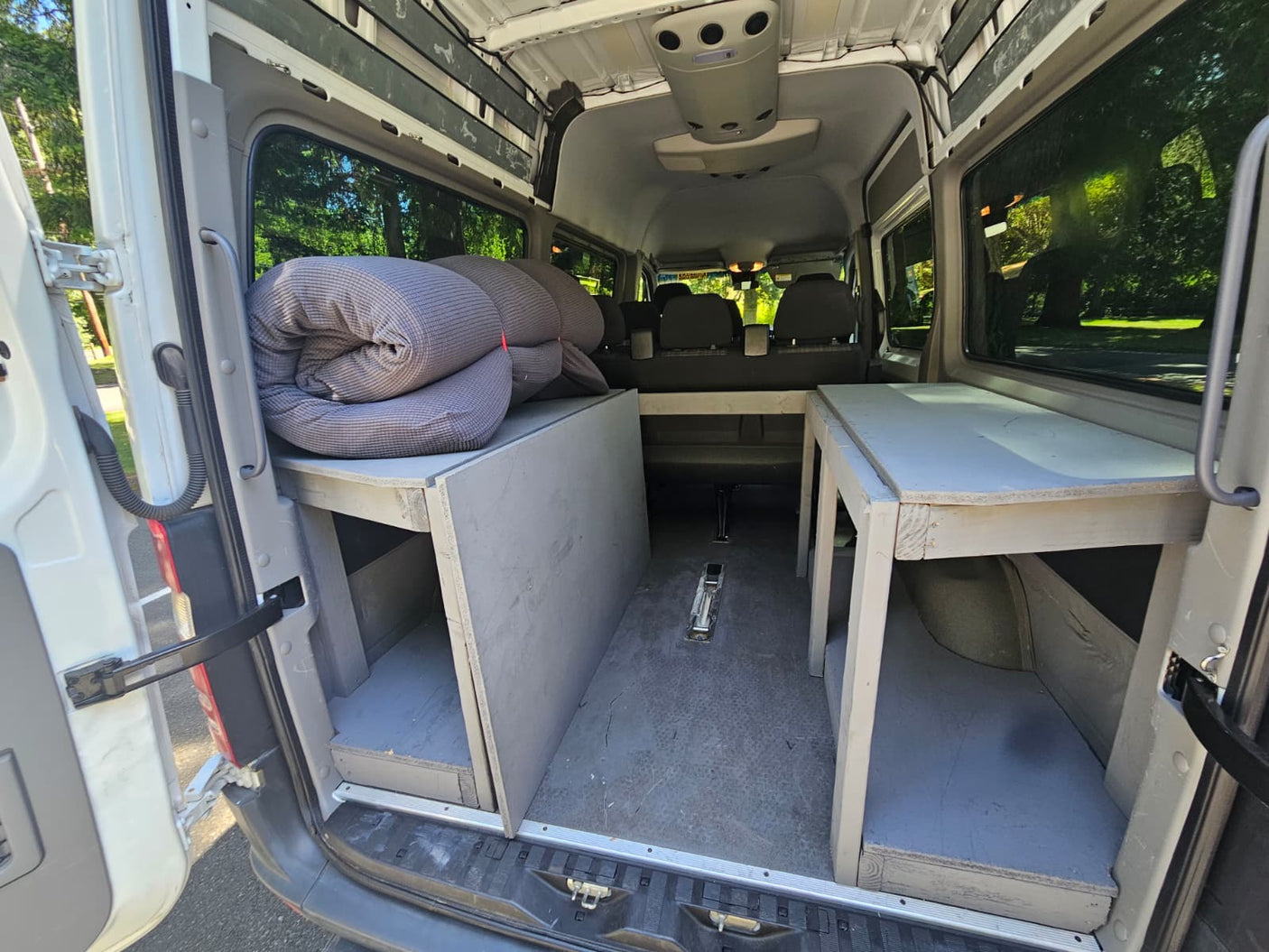RV rental: Inside a camper van with custom wooden storage platforms, rolled bedding, and back seats visible.