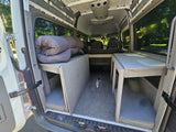 RV rental: Inside a camper van with custom wooden storage platforms, rolled bedding, and back seats visible.