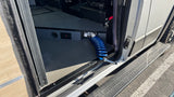 An RV rental van's open side door reveals a utility panel with quick-connect water fittings & a blue coiled wash hose.