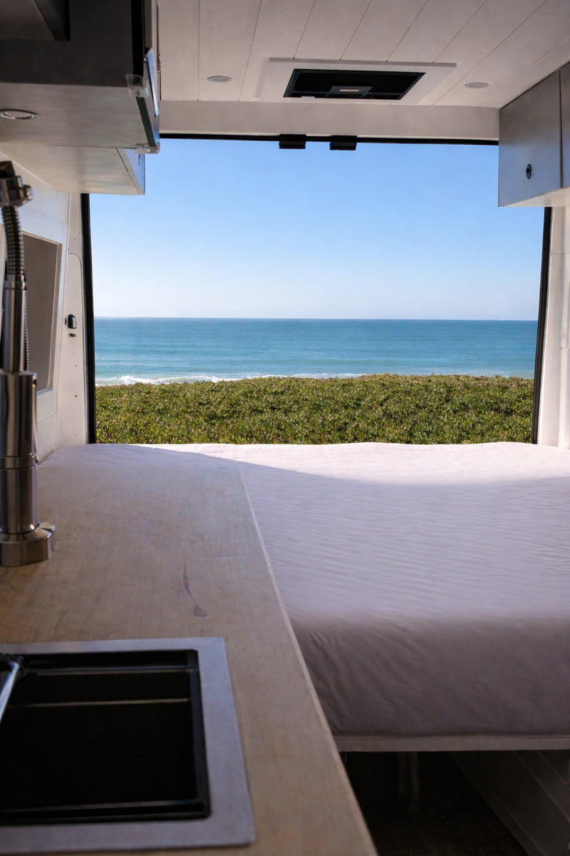  revealing a compact kitchen and person inside prepping food. Ideal for mobile living.|This rv rental showcases a modern camper van interior with a bed — photo 3