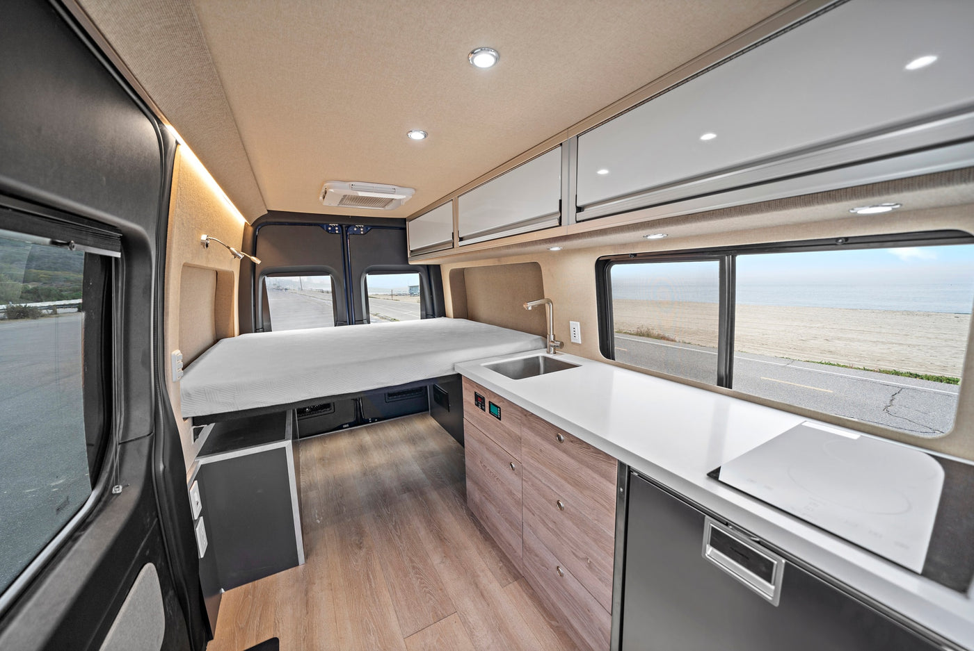 Modern RV rental interior featuring a comfortable bed, full kitchen, and scenic ocean view for your next adventure. — photo 8