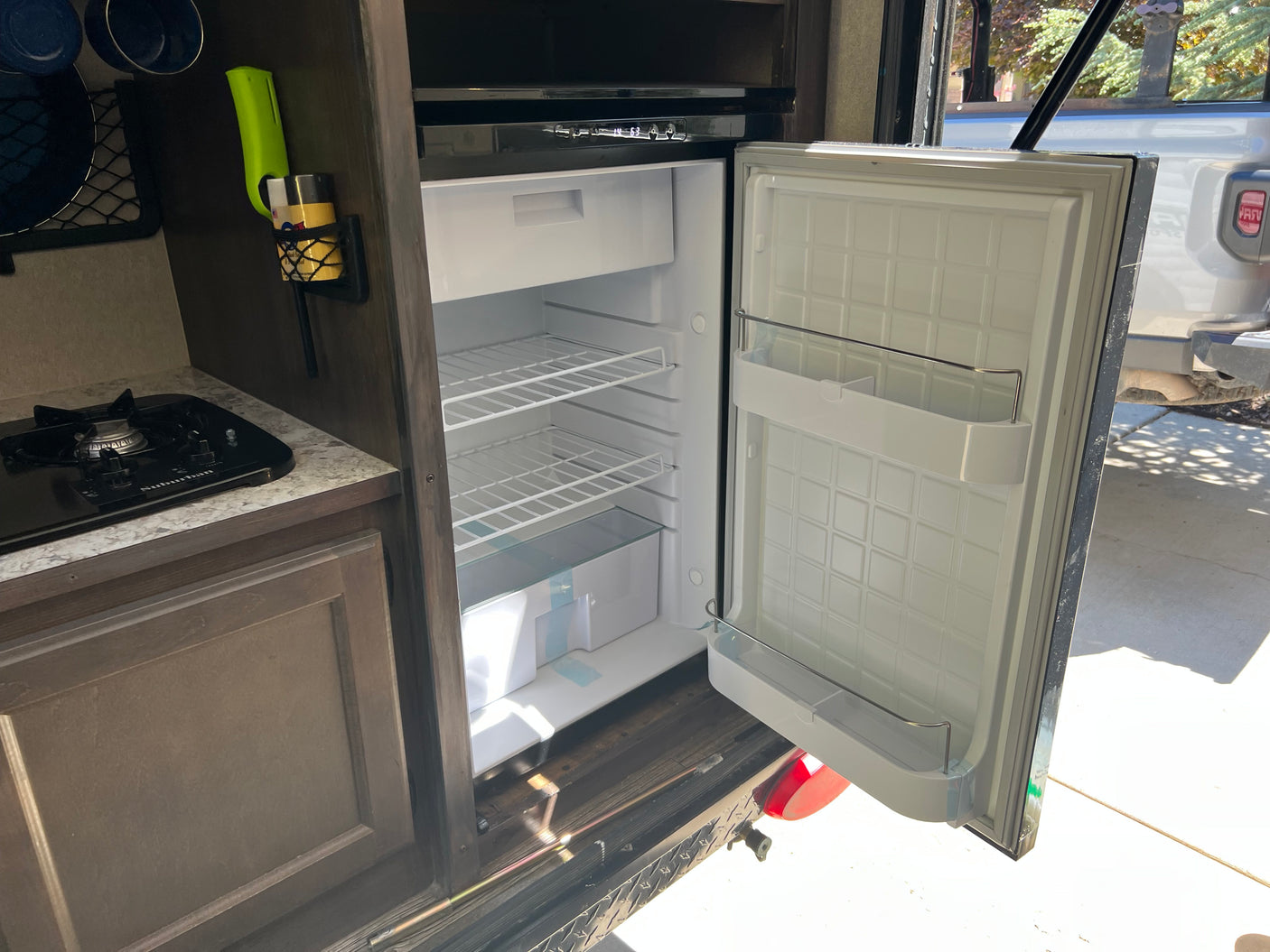 Inside an RV rental: a compact kitchen with an open refrigerator, stovetop, and storage solutions.