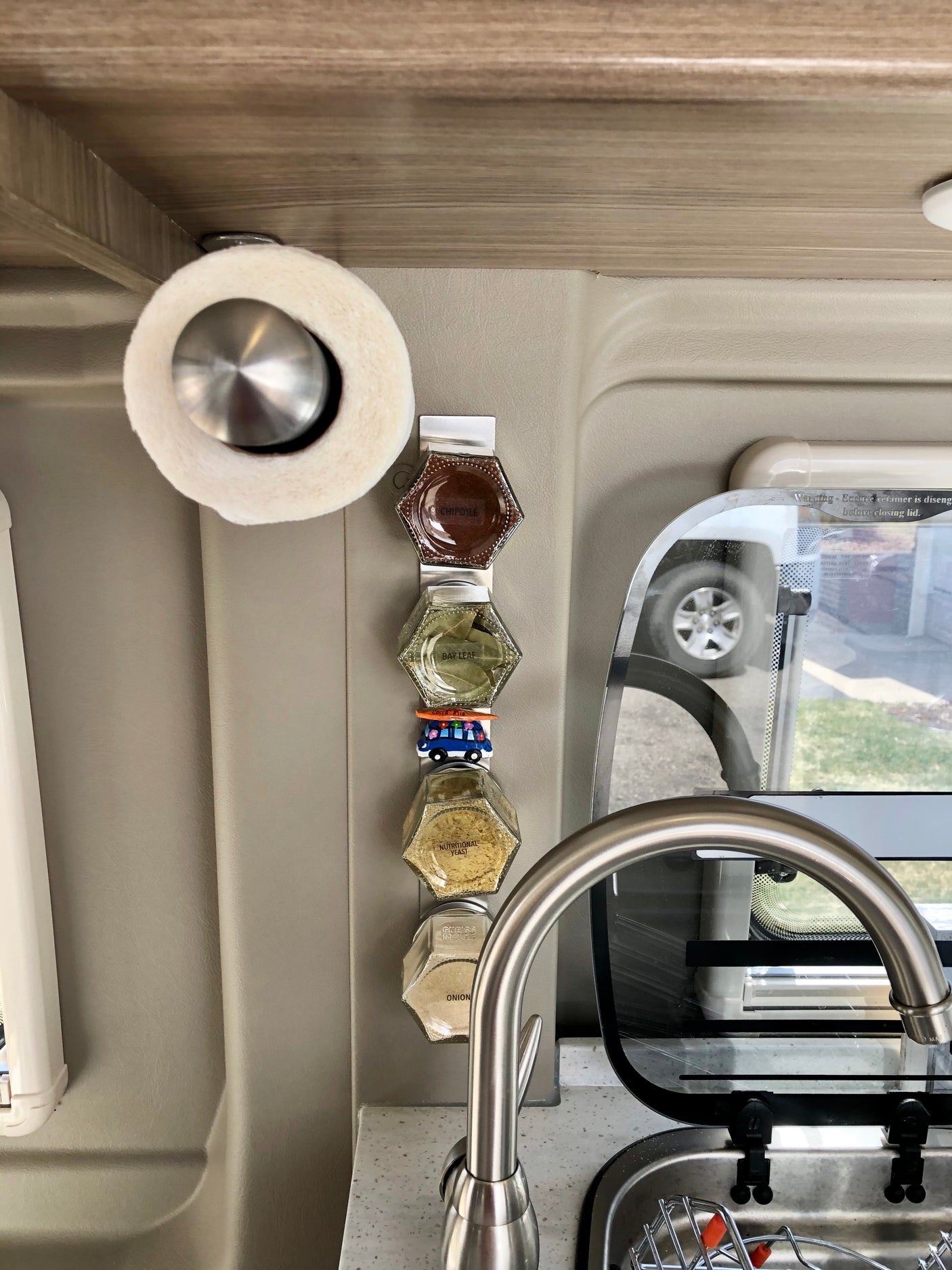 RV rental kitchen area: magnetic spice rack with clearly labeled jars, paper towel holder, and sink. Space-efficient mobile cooking.