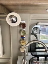 RV rental kitchen area: magnetic spice rack with clearly labeled jars, paper towel holder, and sink. Space-efficient mobile cooking.