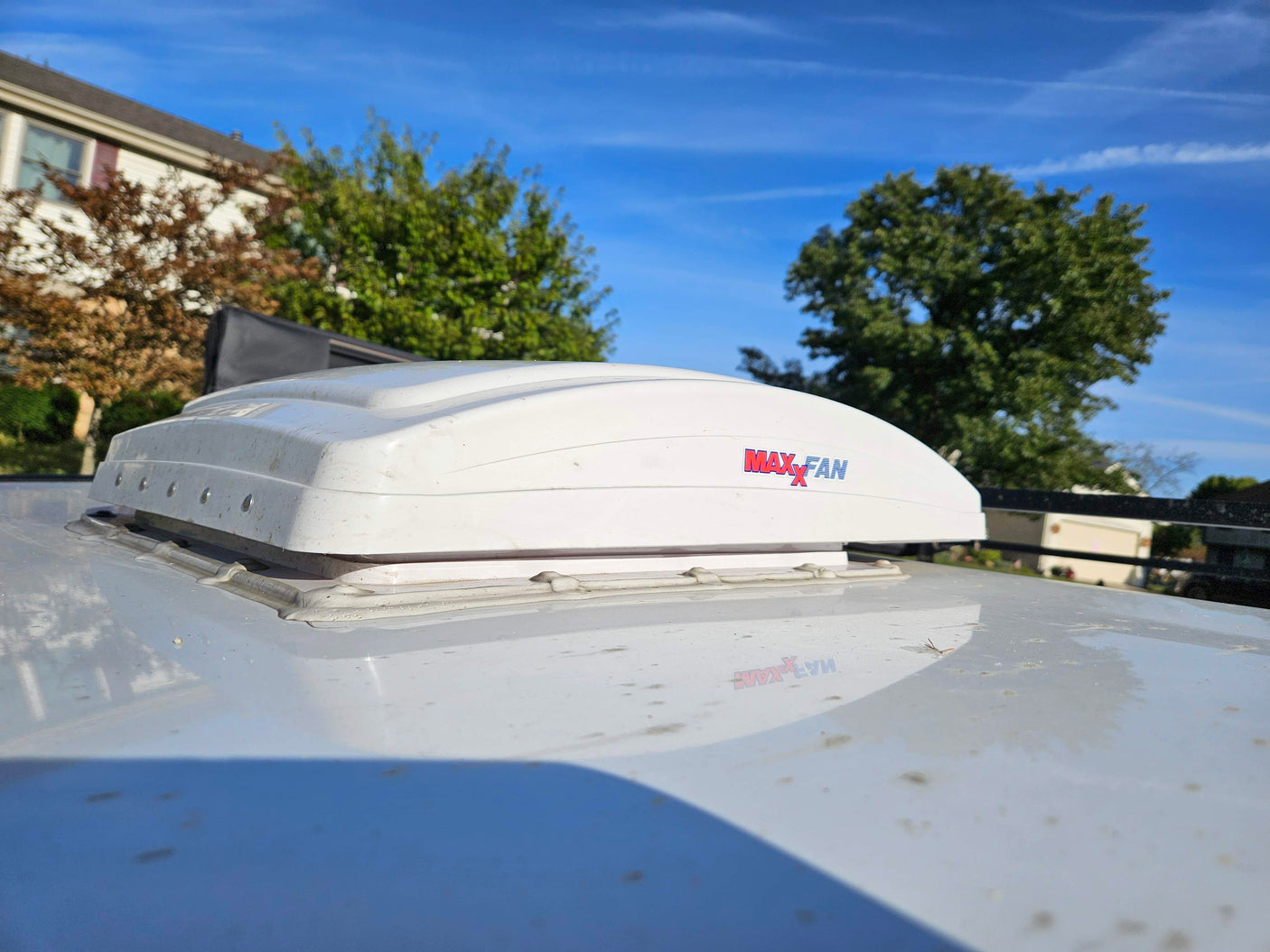 White Maxx Fan vent on an RV rental roof. Close-up shows dirty housing, sealant, and a clear blue sky.