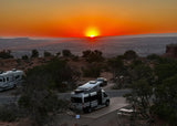Experience adventure! An RV rental and another RV are parked at a desert campsite under a stunning sunset.