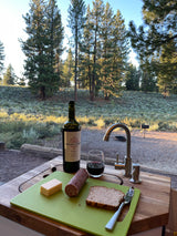 RV rental outdoor kitchen setup with wine, cheese, salami, bread, and forest views.