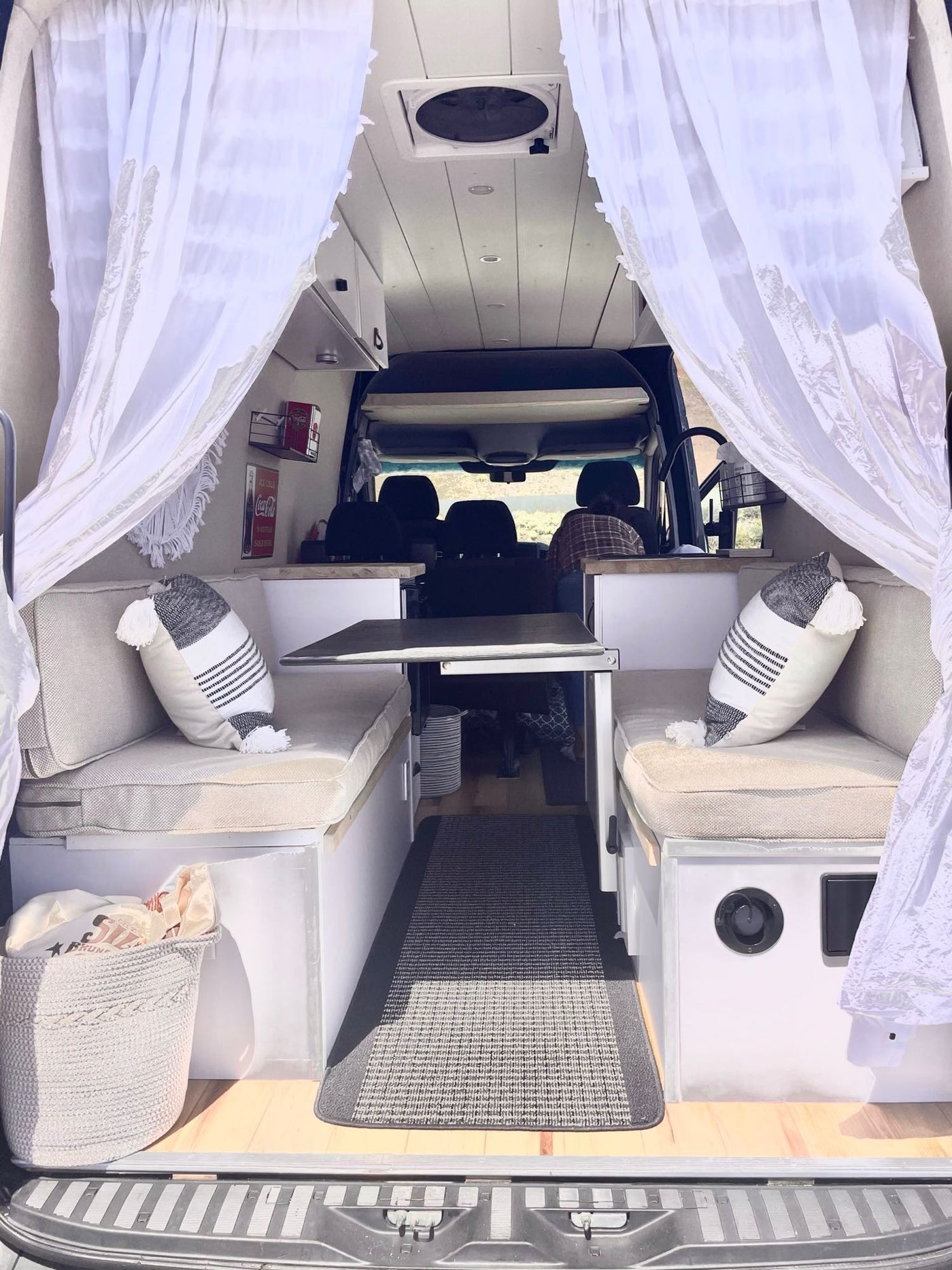 Cozy RV rental interior shows a dinette with benches, table, white curtains. A person is visible in the driver's seat. — photo 4
