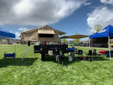 An overland RV rental setup with a deployed rooftop tent and awning at an outdoor event on a sunny day. Perfect for camping!
