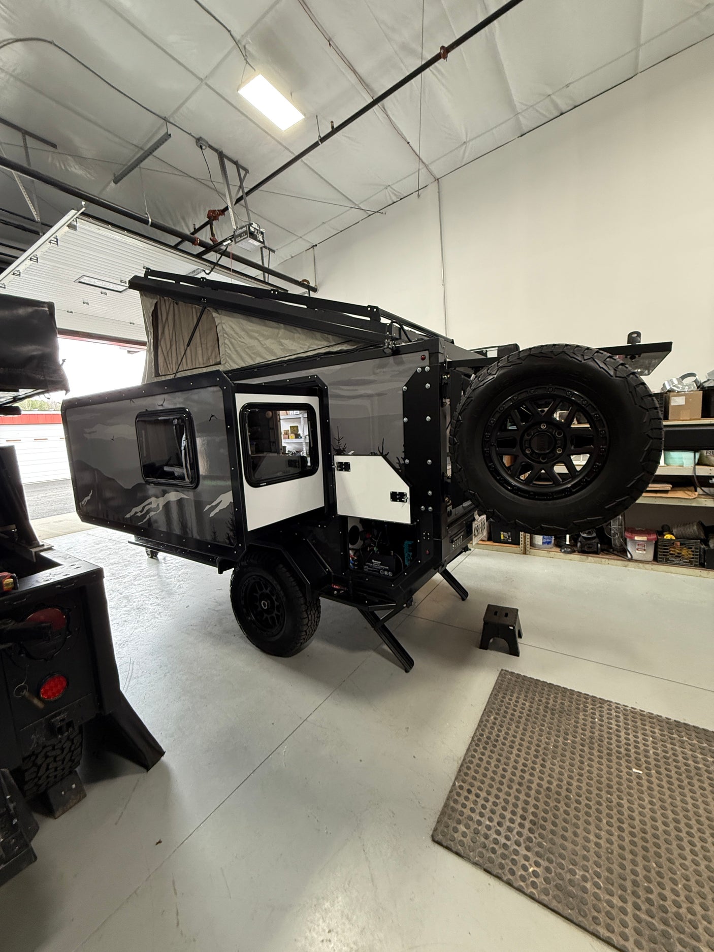 Rugged off-road camper trailer with pop-up tent and spare tire, ideal for an RV rental adventure, parked in a garage.