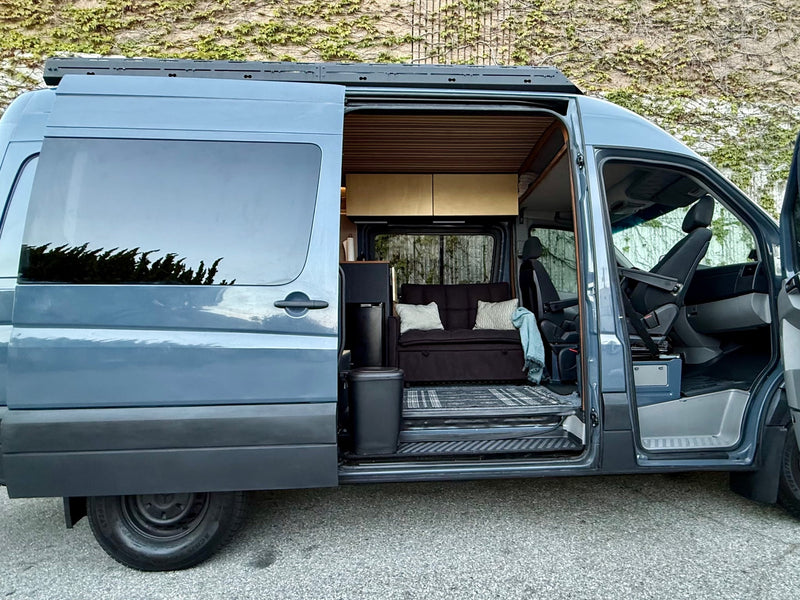  facing a beach and ocean at dusk. Perfect for van life adventures!|This modern blue camper van rv rental opens to a comfortable interior with a sofa — photo 2
