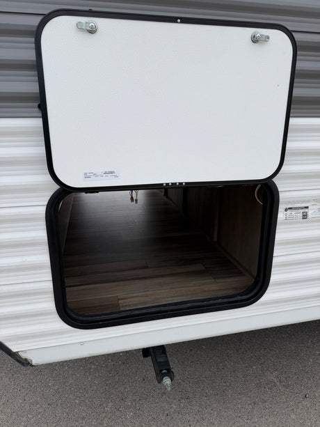 Open exterior storage compartment on an RV rental, revealing a wood-look floor. A leveling jack is seen below.