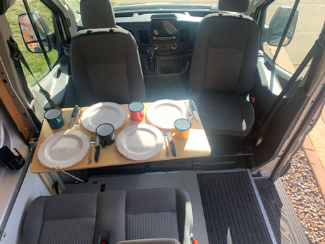 RV rental camper van interior. A dining table for four is set between the front seats and a rear bench, ready for meals.