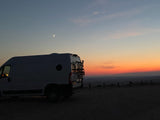 RV rental camper van at a beautiful sunset with a crescent moon, overlooking a scenic landscape, perfect for van life travel.