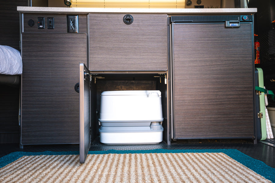 Inside this RV rental: a discreet portable toilet, Isotherm fridge, and power outlets for convenient campervan living.