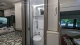 Compact rv rental interior showing bed, bathroom with shower/toilet, and kitchen area with microwave. Perfect for travel.