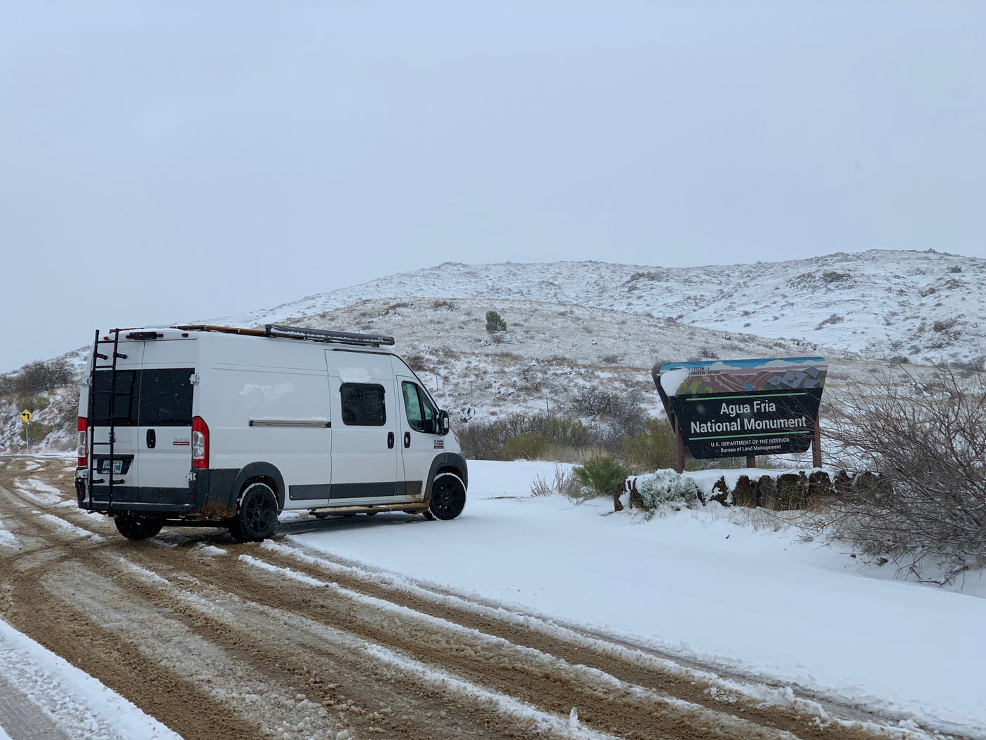 White RV rental parked on a snow-covered dirt road at Agua Fria National Monument during winter.
