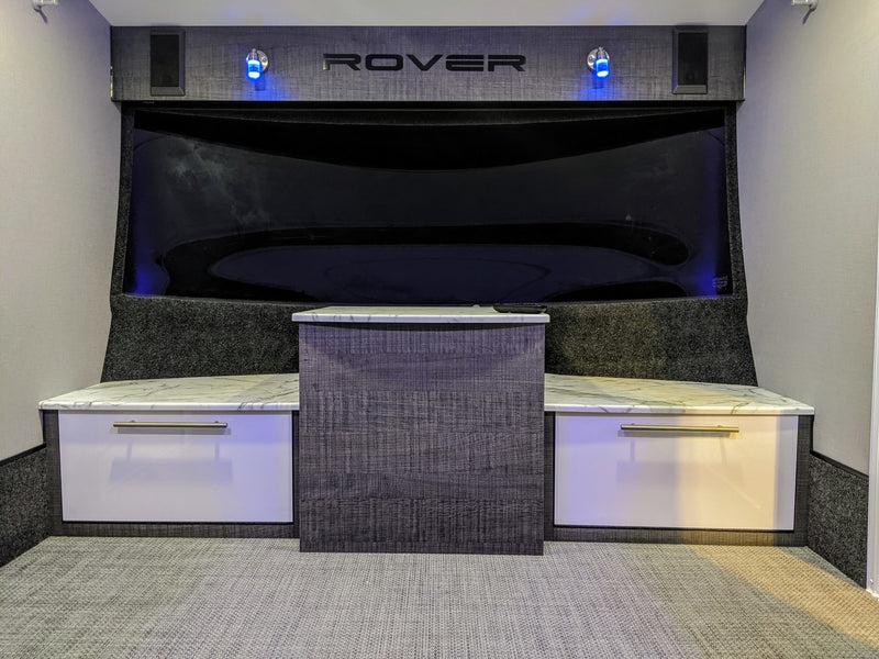 RV rental interior featuring a modern entertainment area with a large dark screen, "ROVER" branding, blue lights, and white/grey cabinets. — photo 8