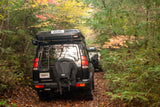 Overland-equipped Land Rover Discovery SUVs, one with a rooftop tent, on a vibrant autumn forest trail. An adventurous RV rental option.