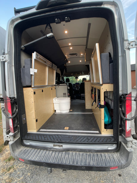 Inside this RV rental: versatile van interior with a folded bed, storage units, and a portable toilet.
