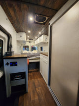An RV rental interior showcasing a wooden ceiling, comfy bed, kitchenette, and built-in cooler for your next trip.
