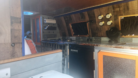 Explore this cozy RV rental's custom van interior featuring a practical kitchen, BODEGA cooler, and comfy living space.