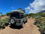 Grey Jeep Wrangler with a Thule Tepui rooftop tent, ideal for an RV rental adventure in Hawaii, parked on a sunny day.