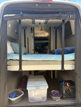 RV rental: Camper van's rear showing a bed, overhead AC, and under-bed storage with supplies.