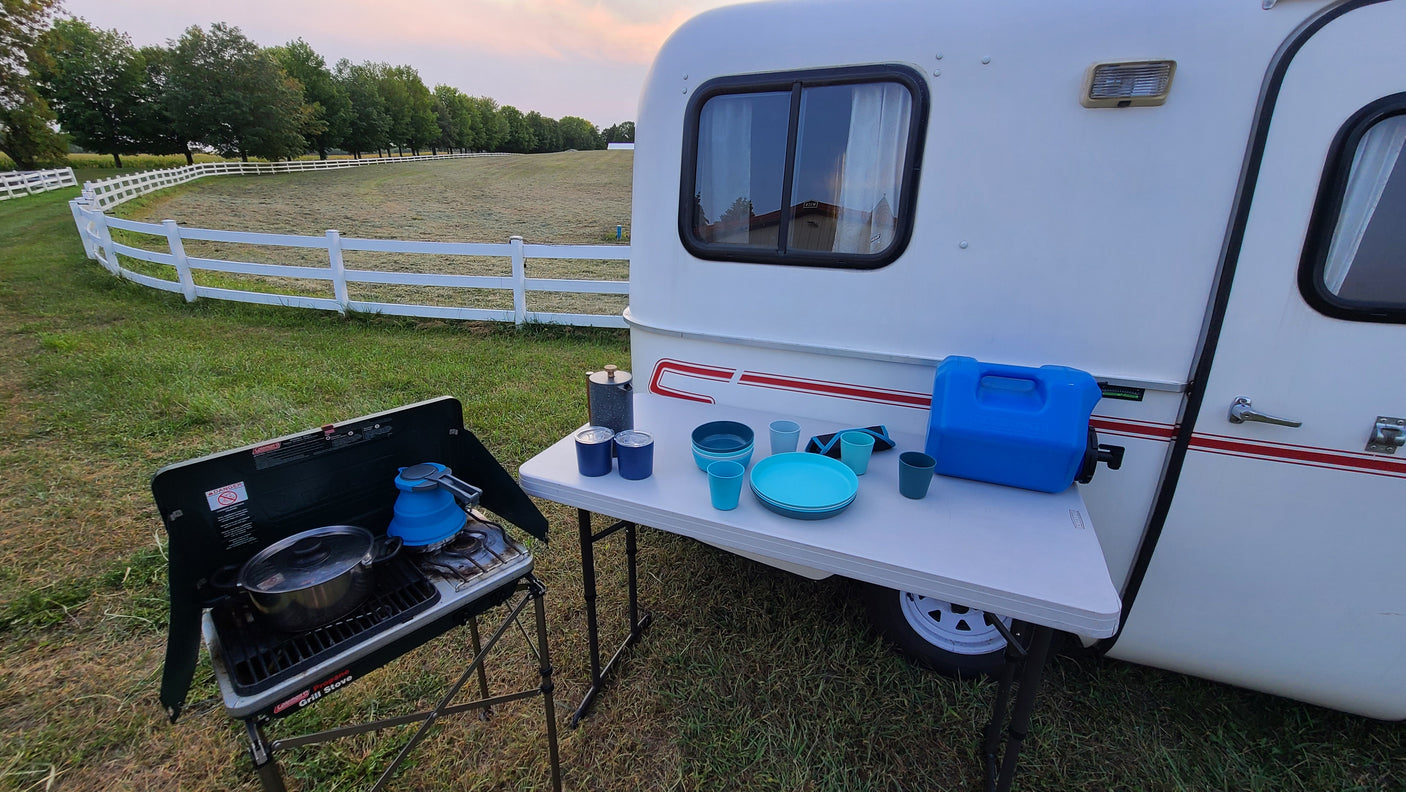 RV rental adventure: camper, outdoor kitchen with stove & table, set against a fenced field at dusk.