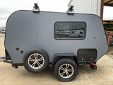 A sleek, grey compact travel trailer, equipped with roof racks and a spare tire, ready for your next rv rental journey.