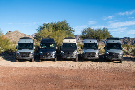 A row of five Mercedes Sprinter camper vans for RV rental, parked in a sunny desert setting.